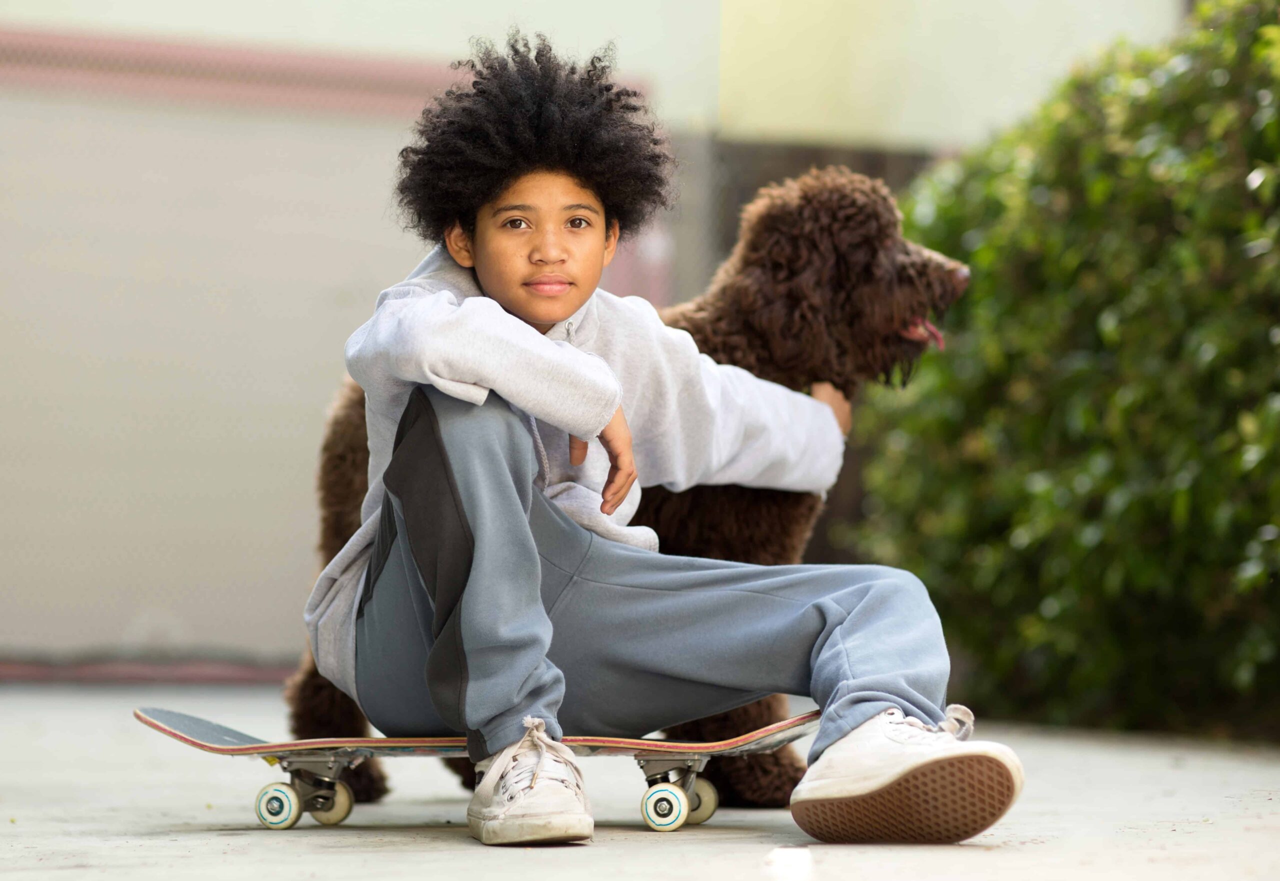 boy around age 12 with brown dog sitting on skateboard